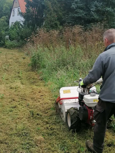 Mann mit Balkenmäher mäht hohes, verwildertes Gras