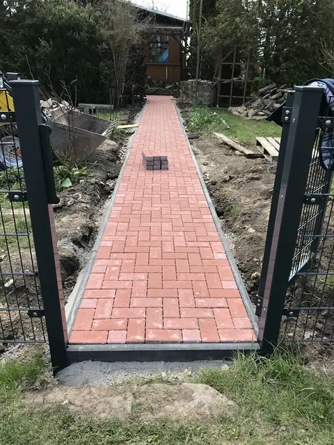 Neu gepflasterter Gartenweg aus roten Klinkern zwischen zwei Torpfosten