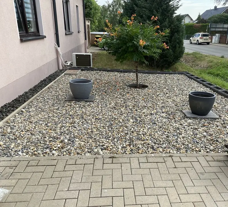 Kiesfläche mit Pflasterrand und Pflanzkübeln vor dem Haus