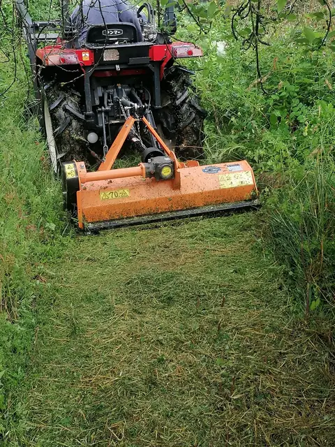 Kleintraktor mit Mulcher arbeitet sich durch hohes Gras