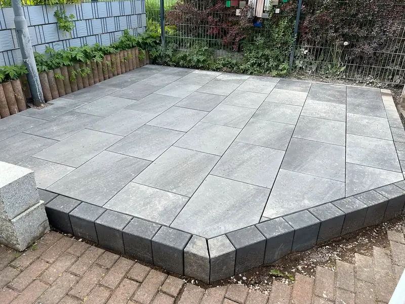 Terrasse aus großen grauen Platten mit Stufe aus dunklen Blockstufen