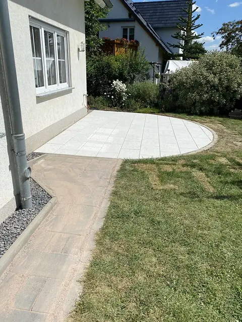 Halbrunde Terrasse aus hellen Platten am Haus, daneben neuer Rasen