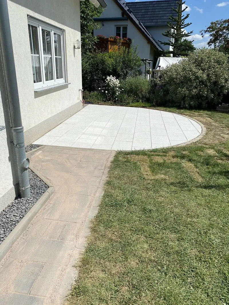 Halbrunde Terrasse aus hellen Platten am Haus, daneben neuer Rasen